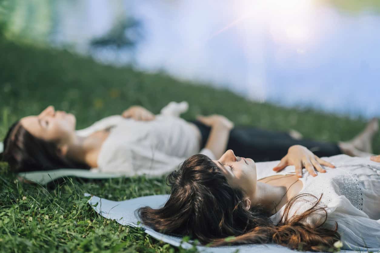 Picture of two women outside, lying on yoga mats and meditating.